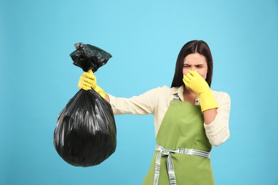 Woman holding full garbage bag on light blue background