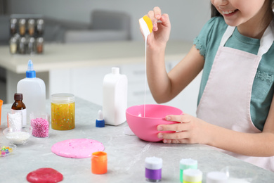 Photo of Little girl mixing ingredients with silicone spatula at table in kitchen, closeup. DIY slime toy