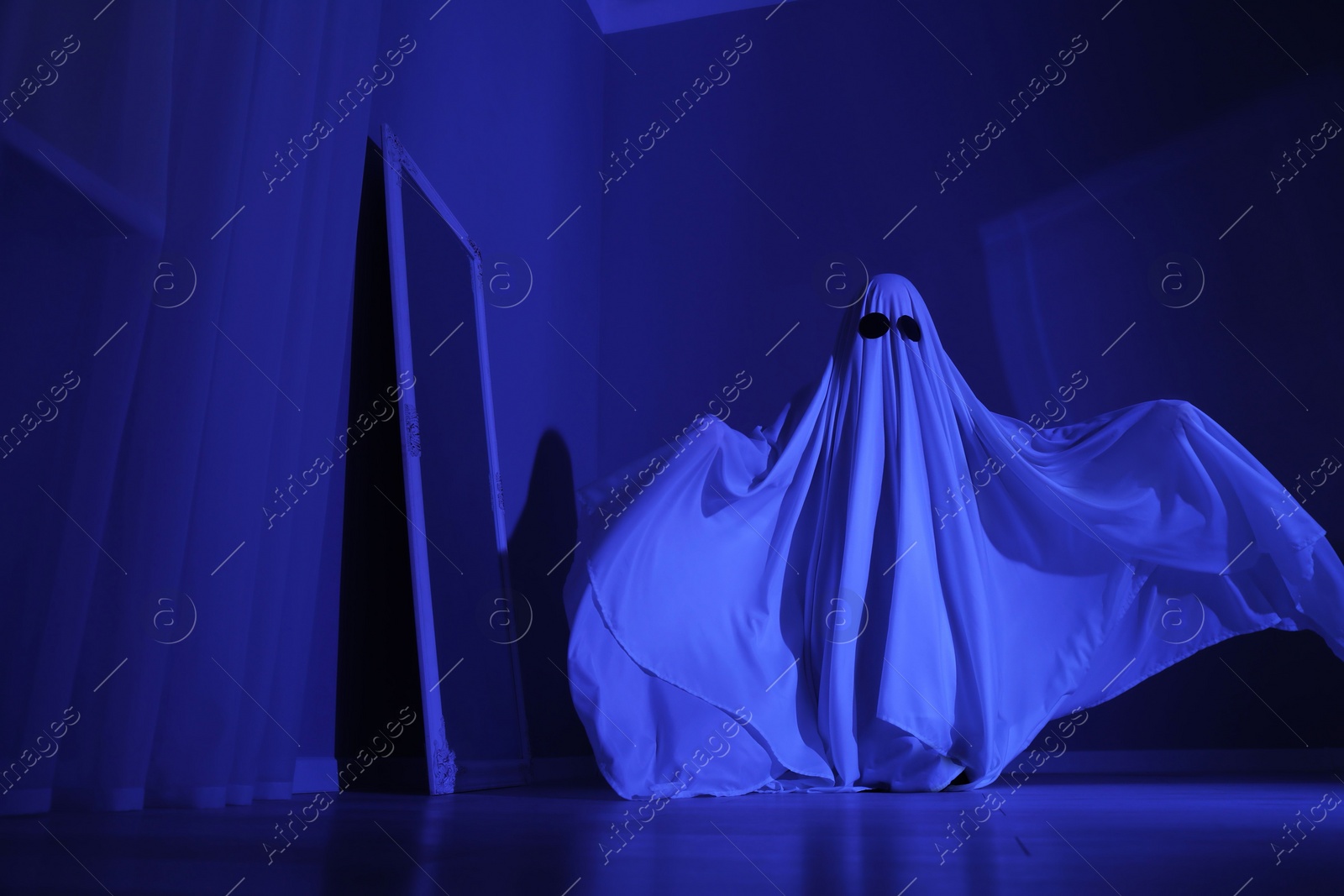 Photo of Creepy ghost. Woman covered with sheet in blue light, low angle view