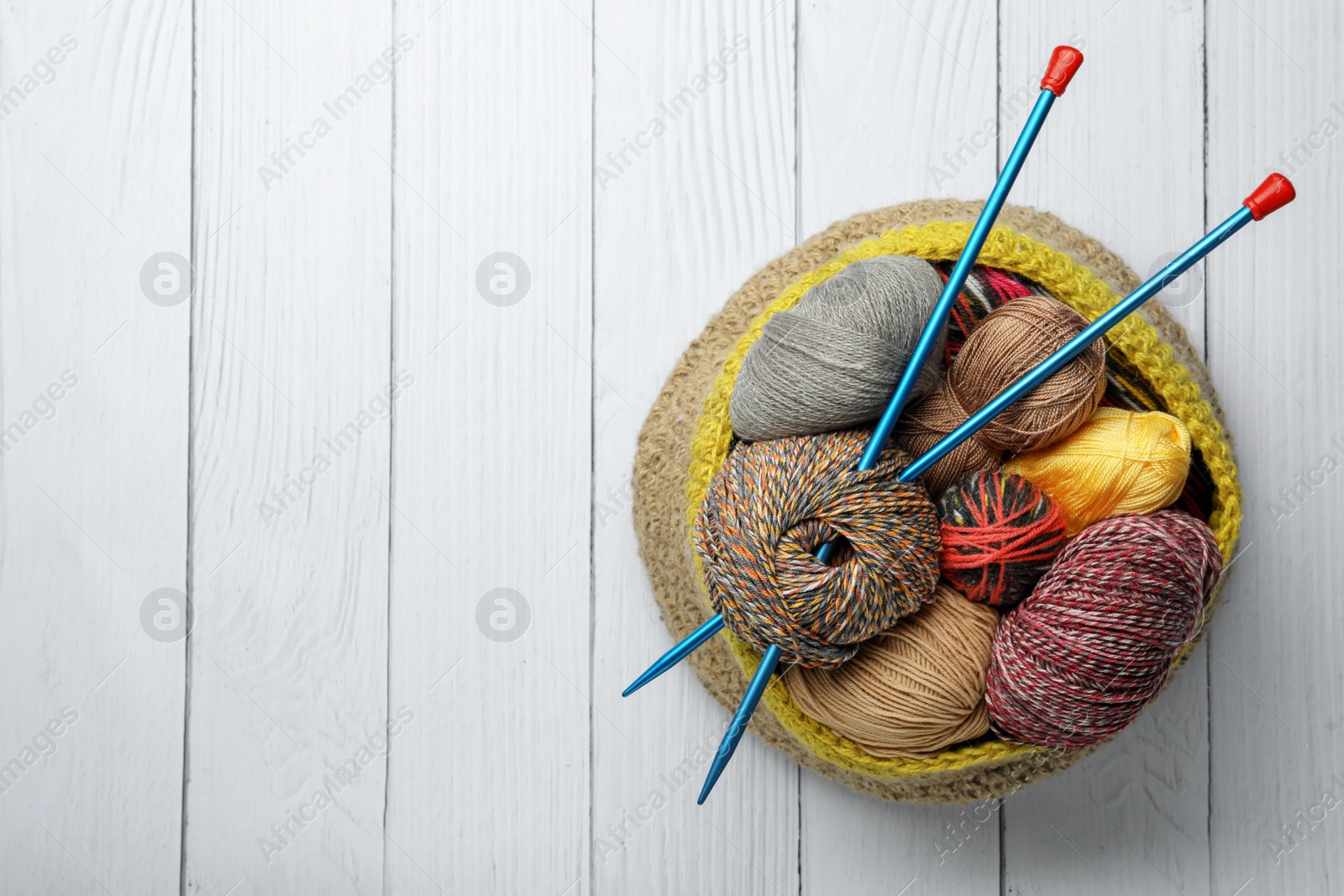 Photo of Soft woolen yarns and knitting needles on white wooden table, top view. Space for text