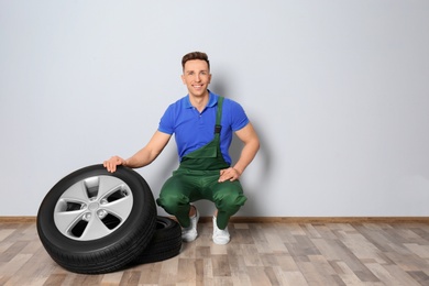 Male mechanic with car tires on light wall background