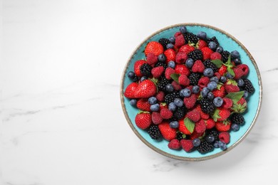 Photo of Many different fresh ripe berries in bowl on white table, top view. Space for text