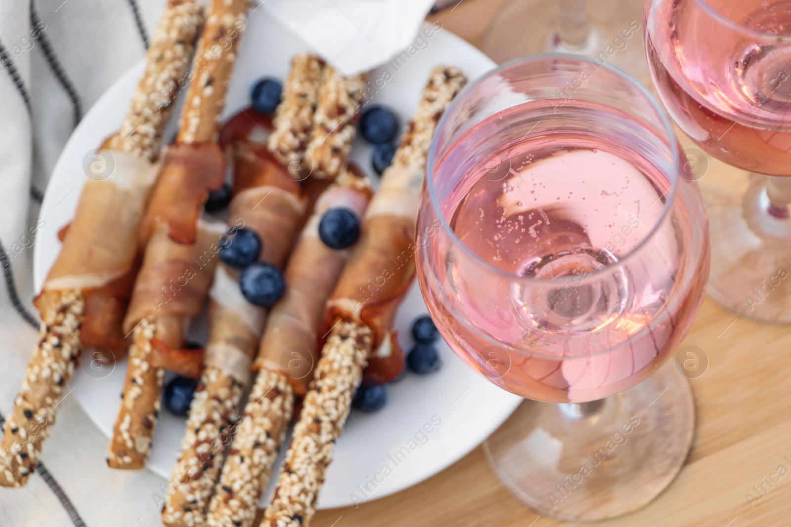 Photo of Glasses of delicious rose wine and food on white picnic blanket, closeup