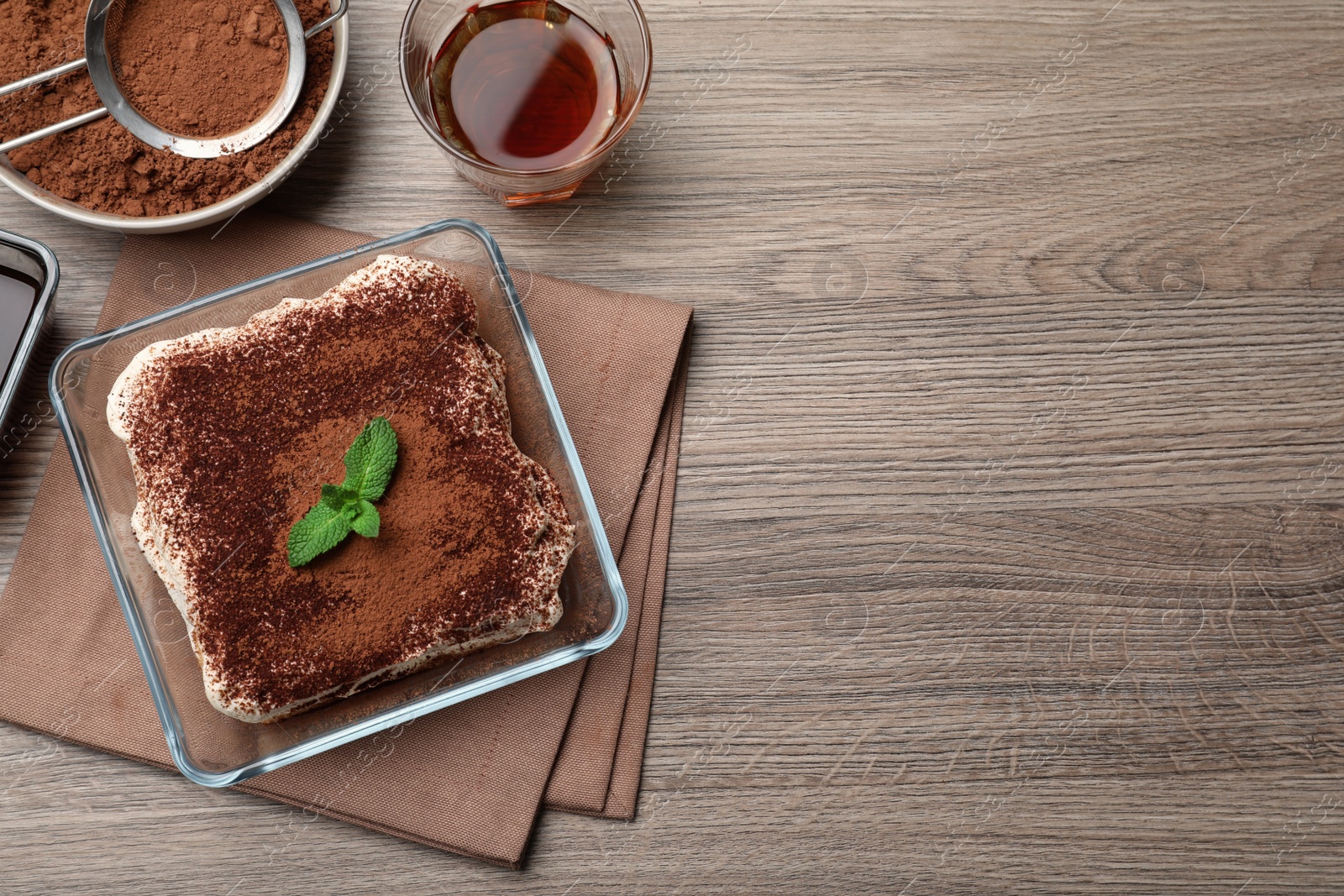 Photo of Glass bowl with delicious tiramisu cake on wooden table, flat lay. Space for text
