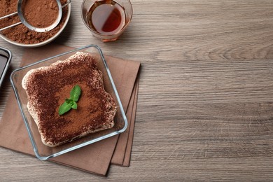 Glass bowl with delicious tiramisu cake on wooden table, flat lay. Space for text