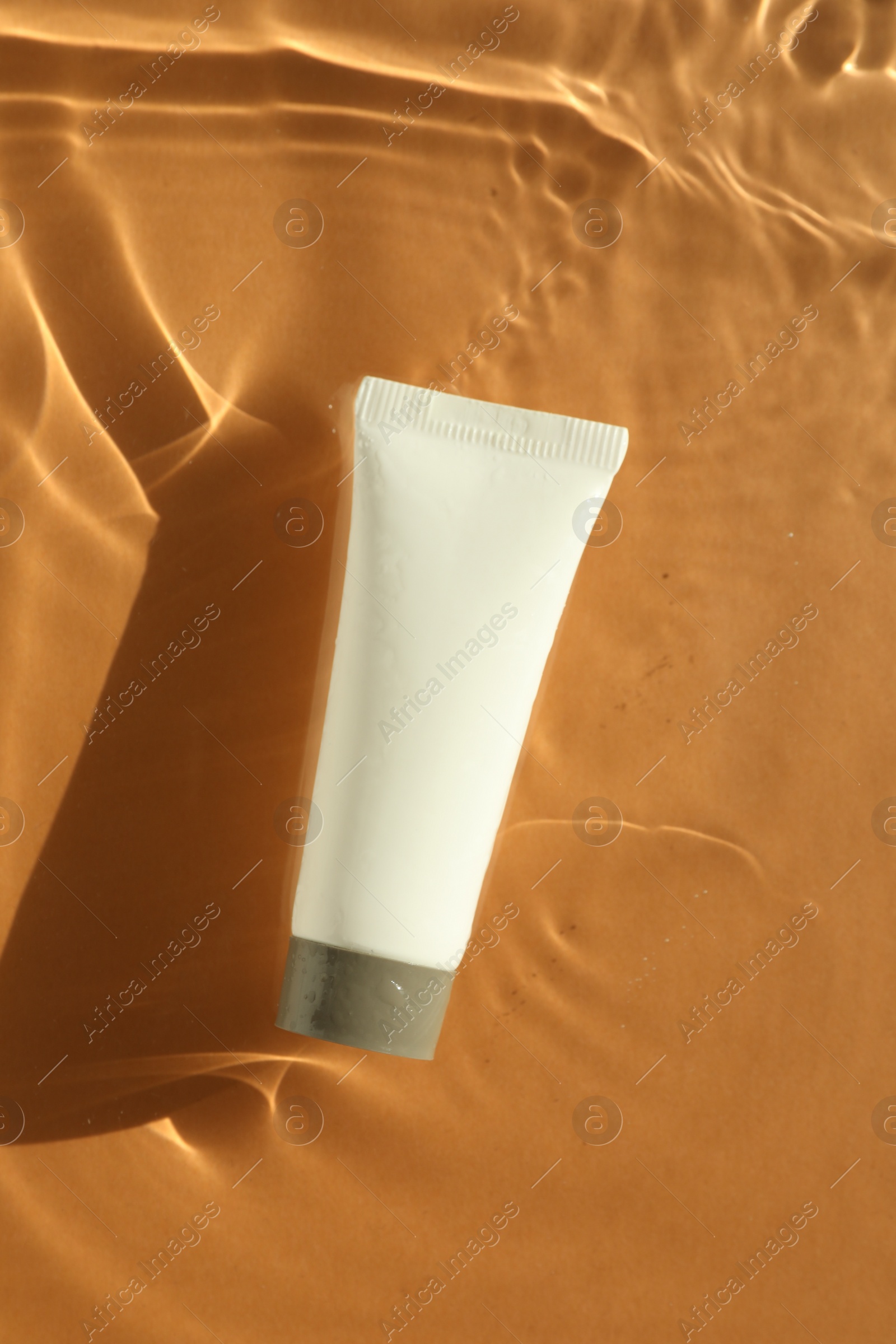 Photo of Tube with moisturizing cream in water on orange background, top view