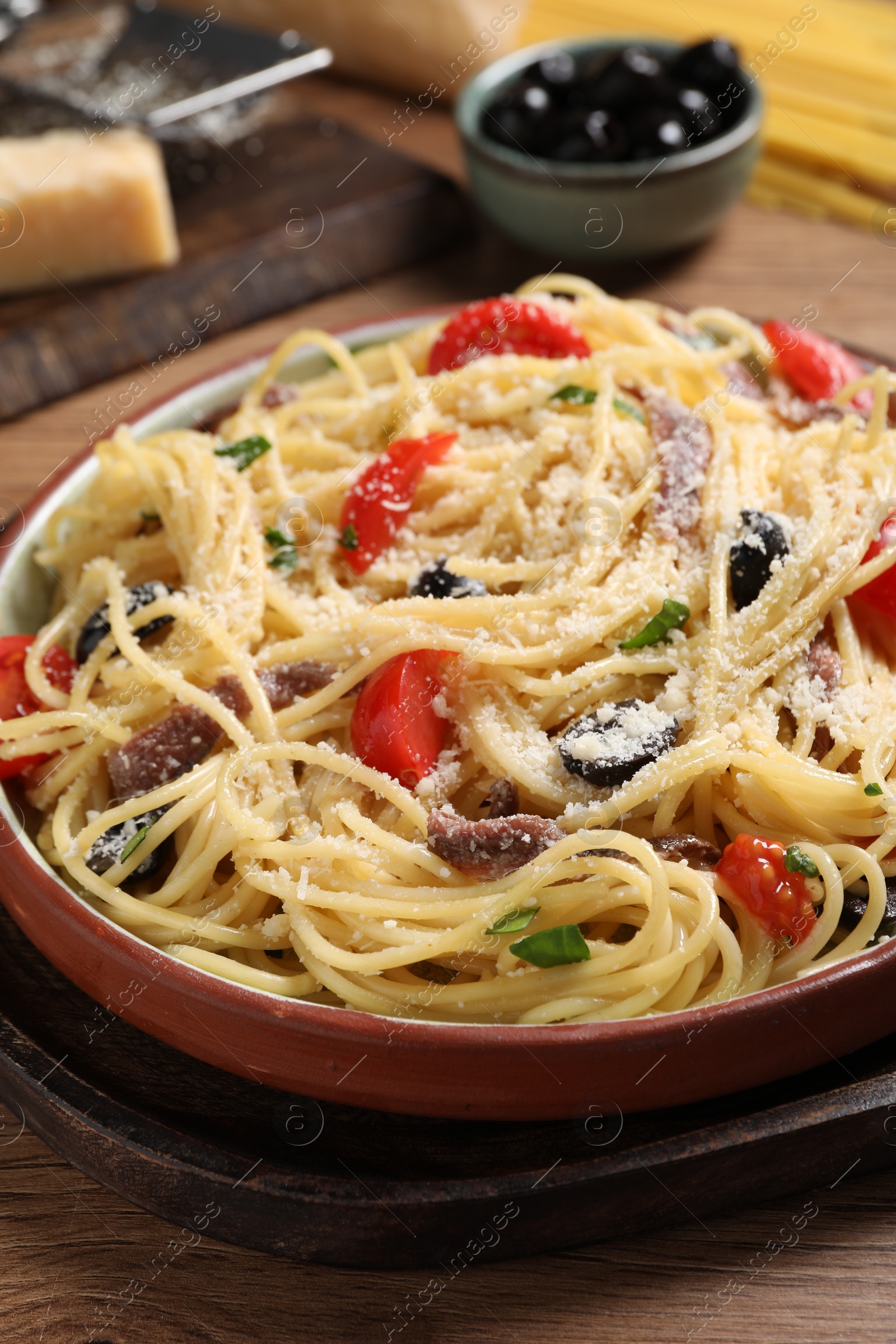 Photo of Delicious pasta with anchovies, tomatoes and parmesan cheese served on wooden table, closeup