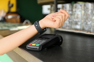Photo of Woman using smartwatch for contactless payment at bar counter, closeup