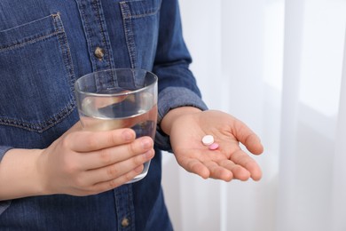 Photo of Woman with glass of water and pill indoors, closeup