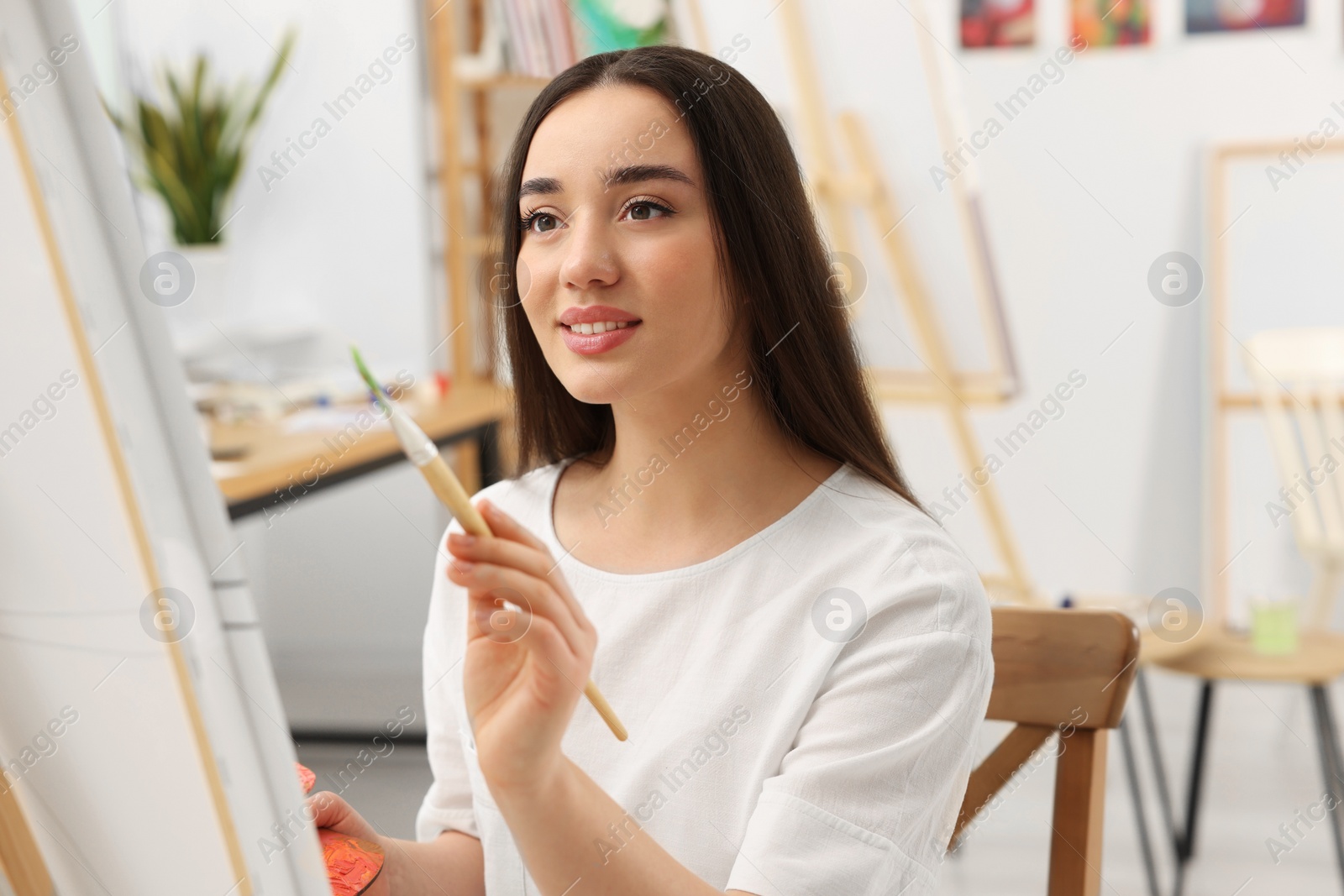 Photo of Beautiful young woman painting with brush in studio. Creative hobby