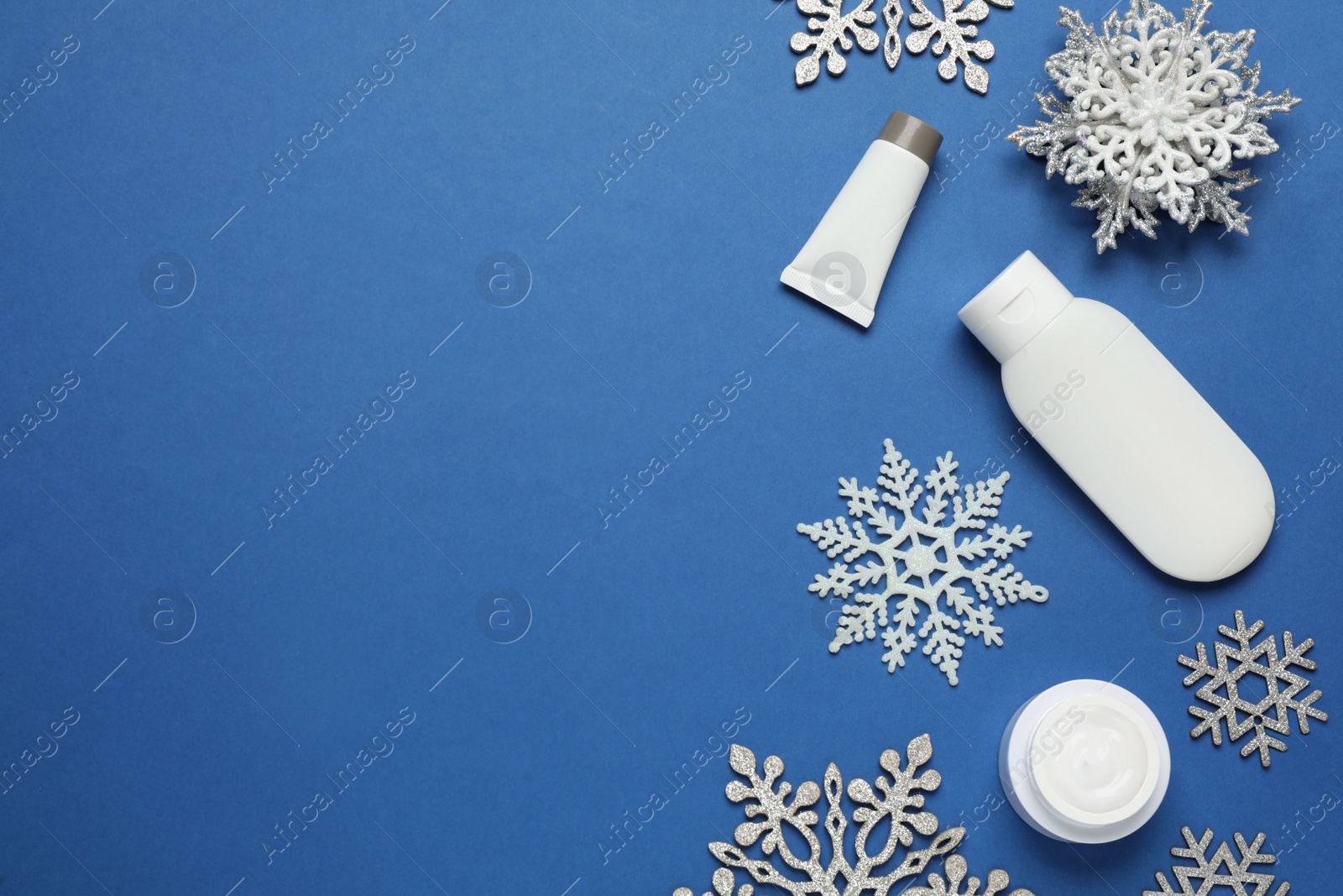 Photo of Flat lay composition with cosmetic products and snowflakes on blue background, space for text. Winter skin care