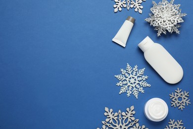 Flat lay composition with cosmetic products and snowflakes on blue background, space for text. Winter skin care