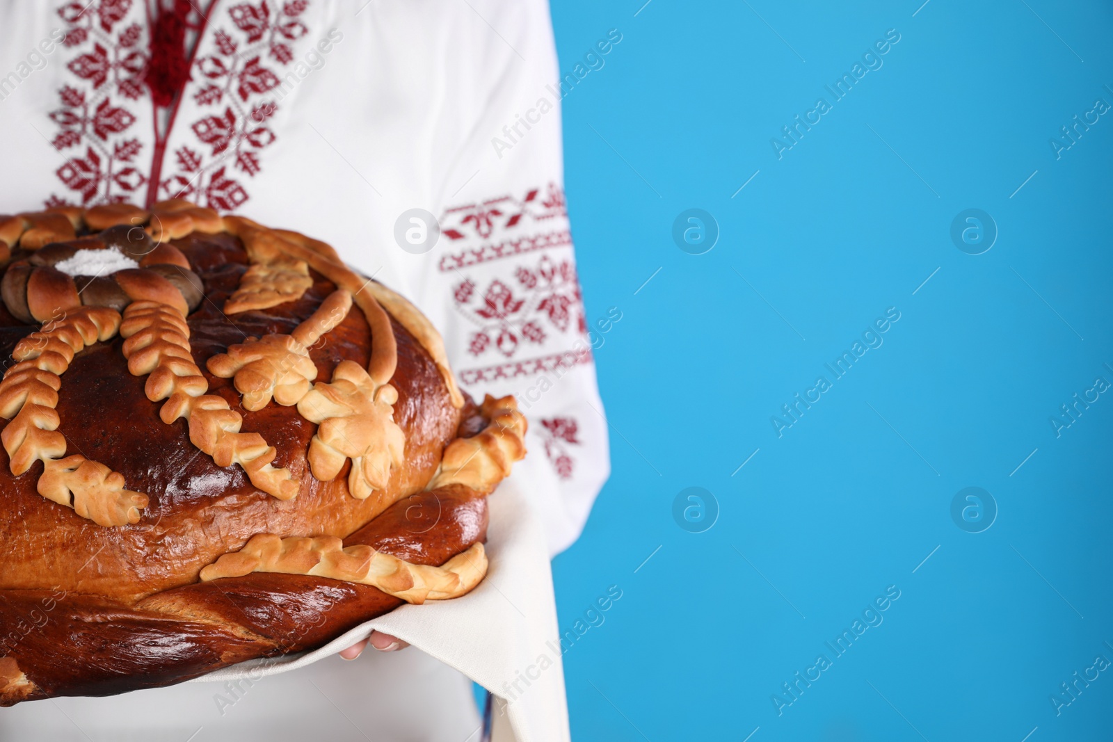 Photo of Woman holding korovai on light blue background, closeup with space for text. Ukrainian bread and salt welcoming tradition