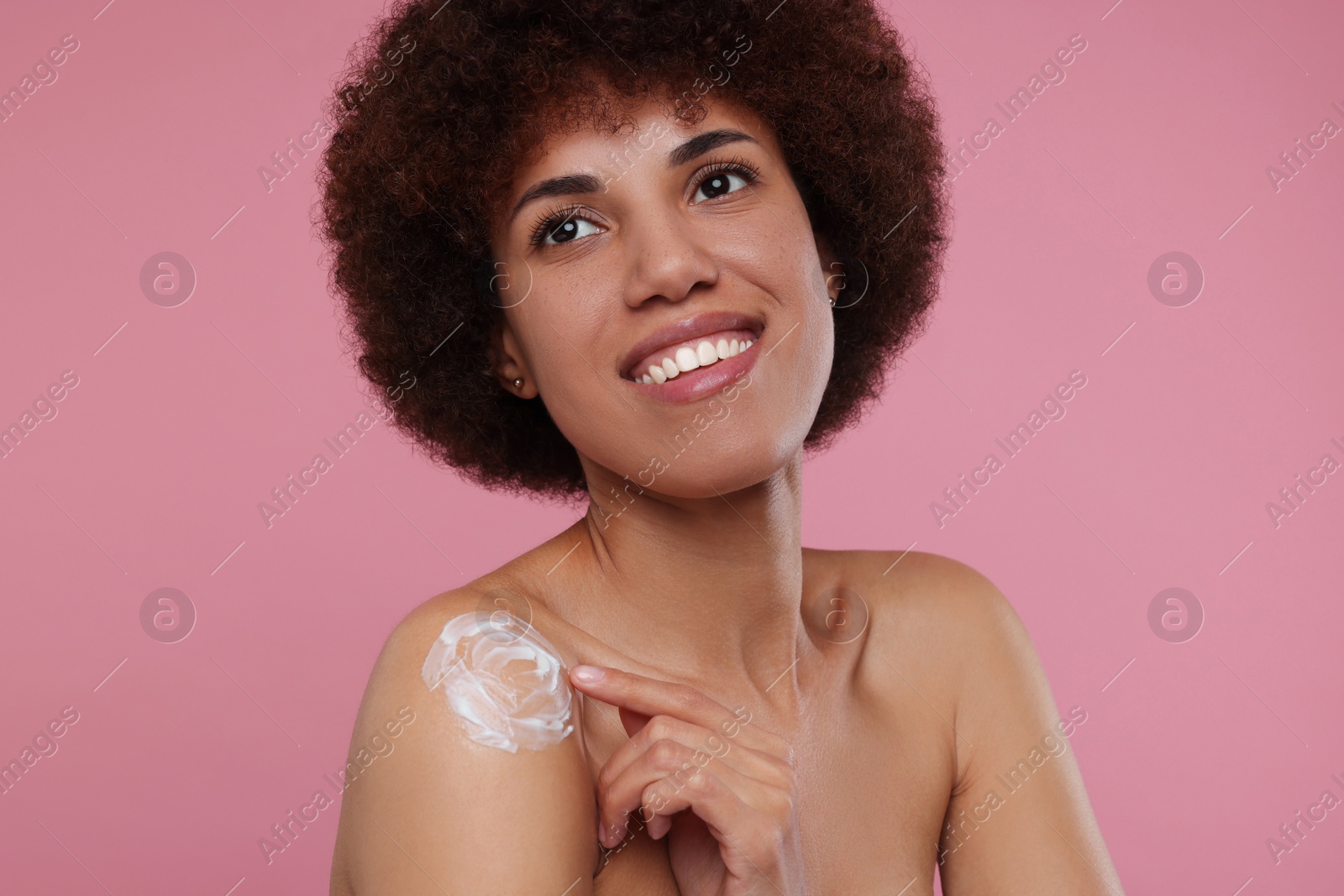 Photo of Beautiful young woman applying body cream onto shoulder on pink background