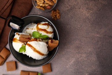 Bowl of tasty ice cream with caramel sauce, candies and mint on brown table, flat lay. Space for text