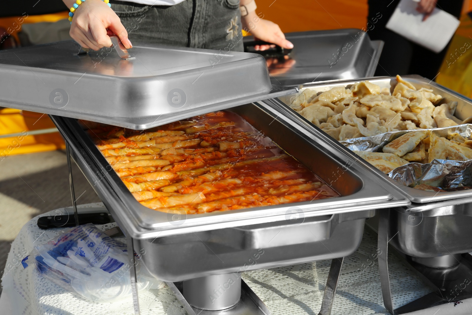 Photo of Female volunteer distributing delicious stuffed cabbage, dumplings and patties from food warmers