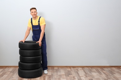 Male mechanic with car tires on light wall background