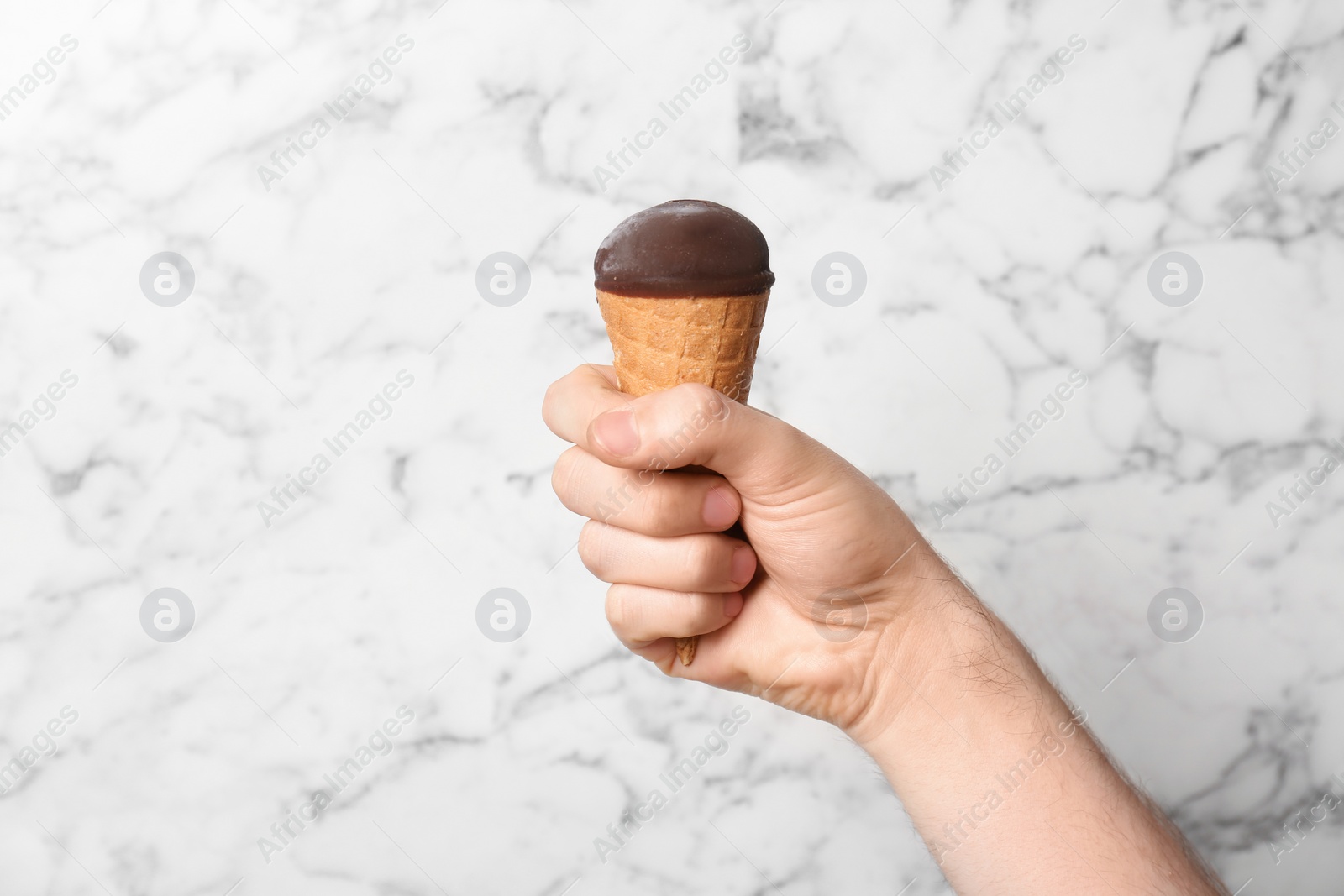 Photo of Man holding yummy ice cream on marble background. Focus on hand