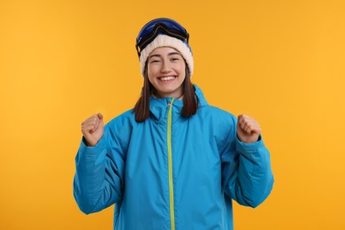 Winter sports. Excited woman with snowboard goggles on orange background