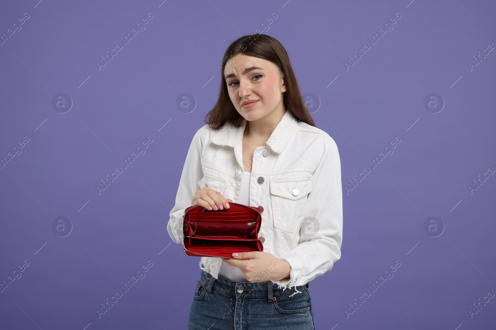 Photo of Sad woman showing empty wallet on purple background