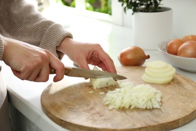 Photo of Woman chopping white onion on wooden board at table, closeup