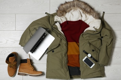 Set of warm clothes and devices on wooden background, flat lay. Winter vacation