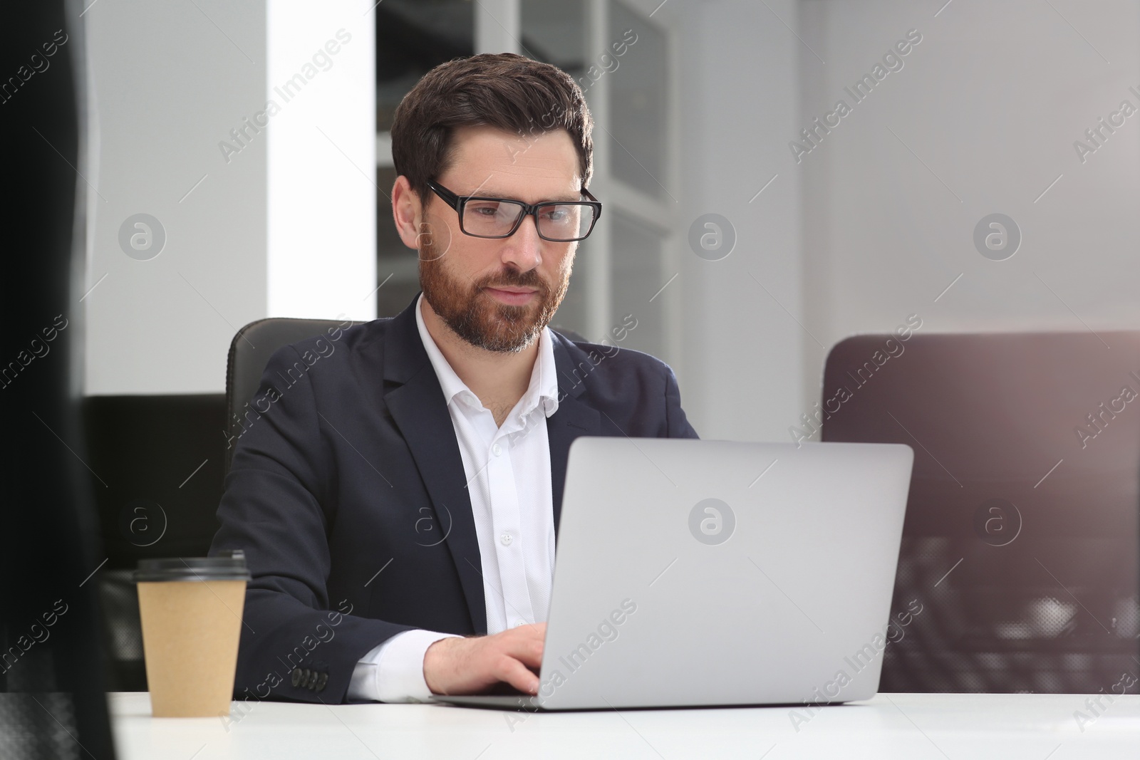 Photo of Man working on laptop at white desk in office