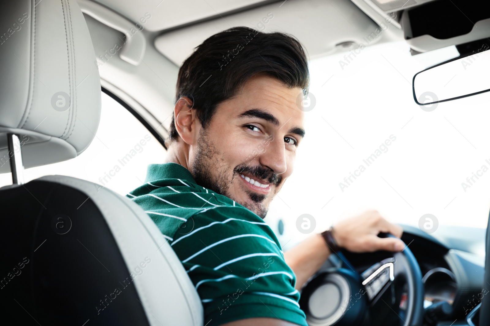 Photo of Attractive young man driving luxury car, view from backseat