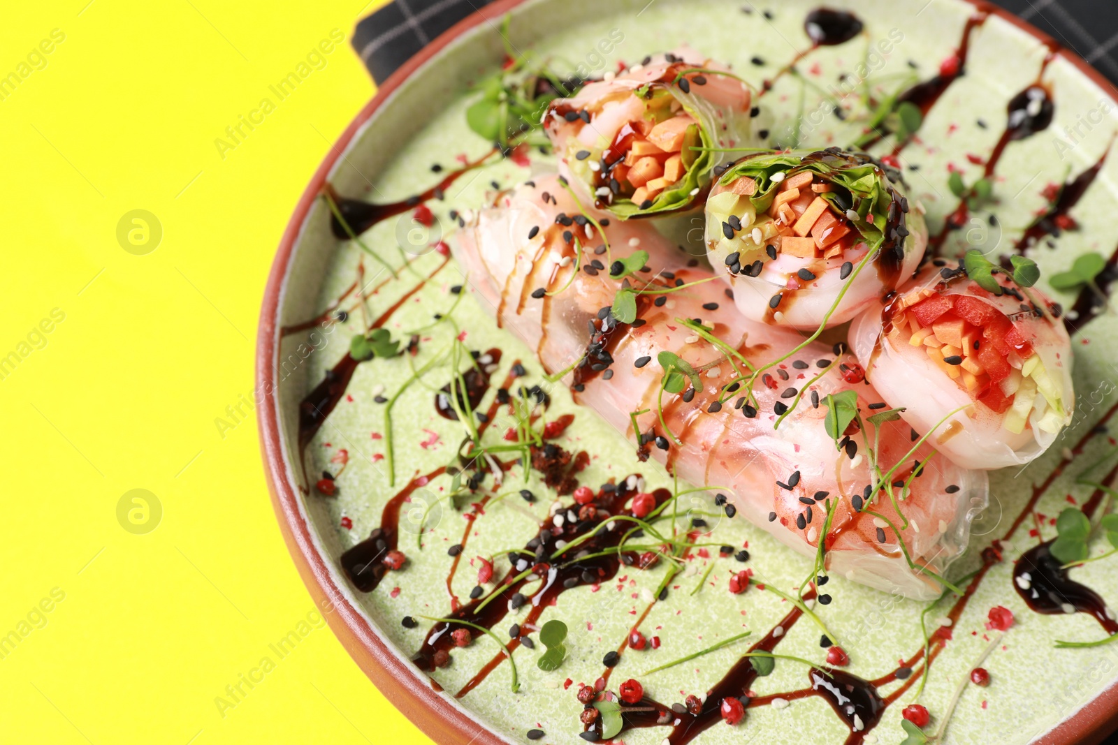 Photo of Plate of delicious spring rolls with sauce and microgreens on yellow background, closeup