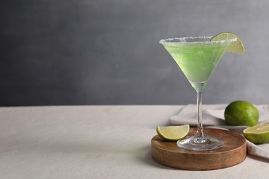 Photo of Delicious Margarita cocktail in glass and limes on light table, space for text