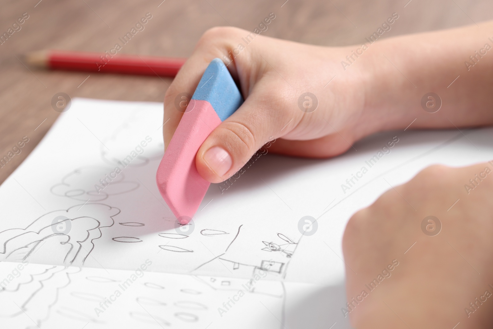 Photo of Girl erasing drawing in her book at wooden table, closeup