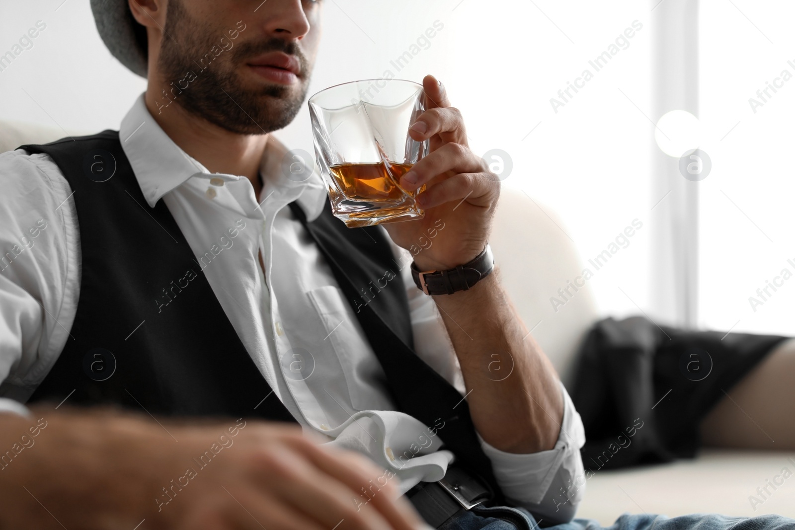 Photo of Young man with glass of whiskey sitting on sofa at home, closeup