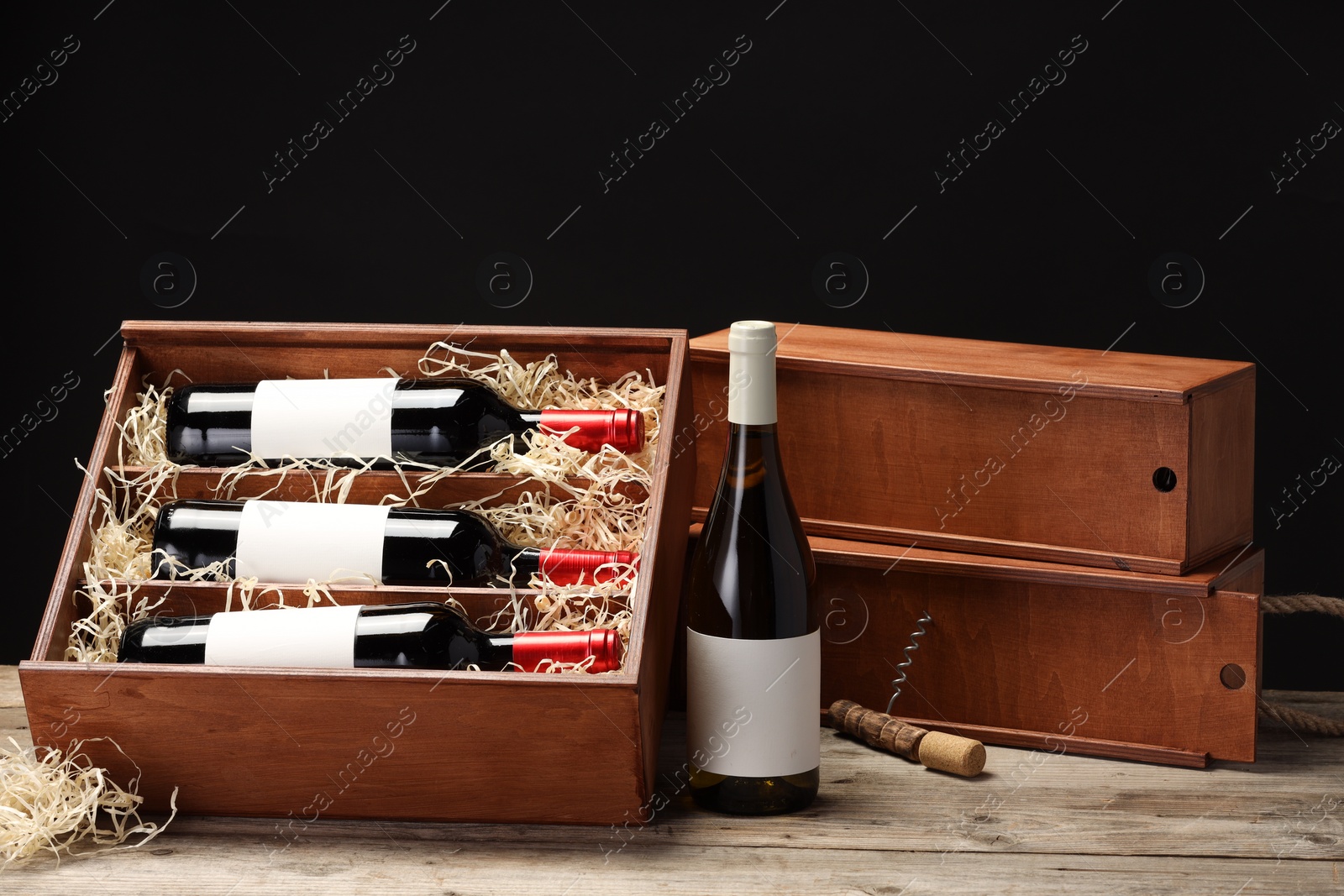 Photo of Box with wine bottles and corkscrew on wooden table against black background