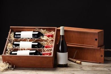 Box with wine bottles and corkscrew on wooden table against black background