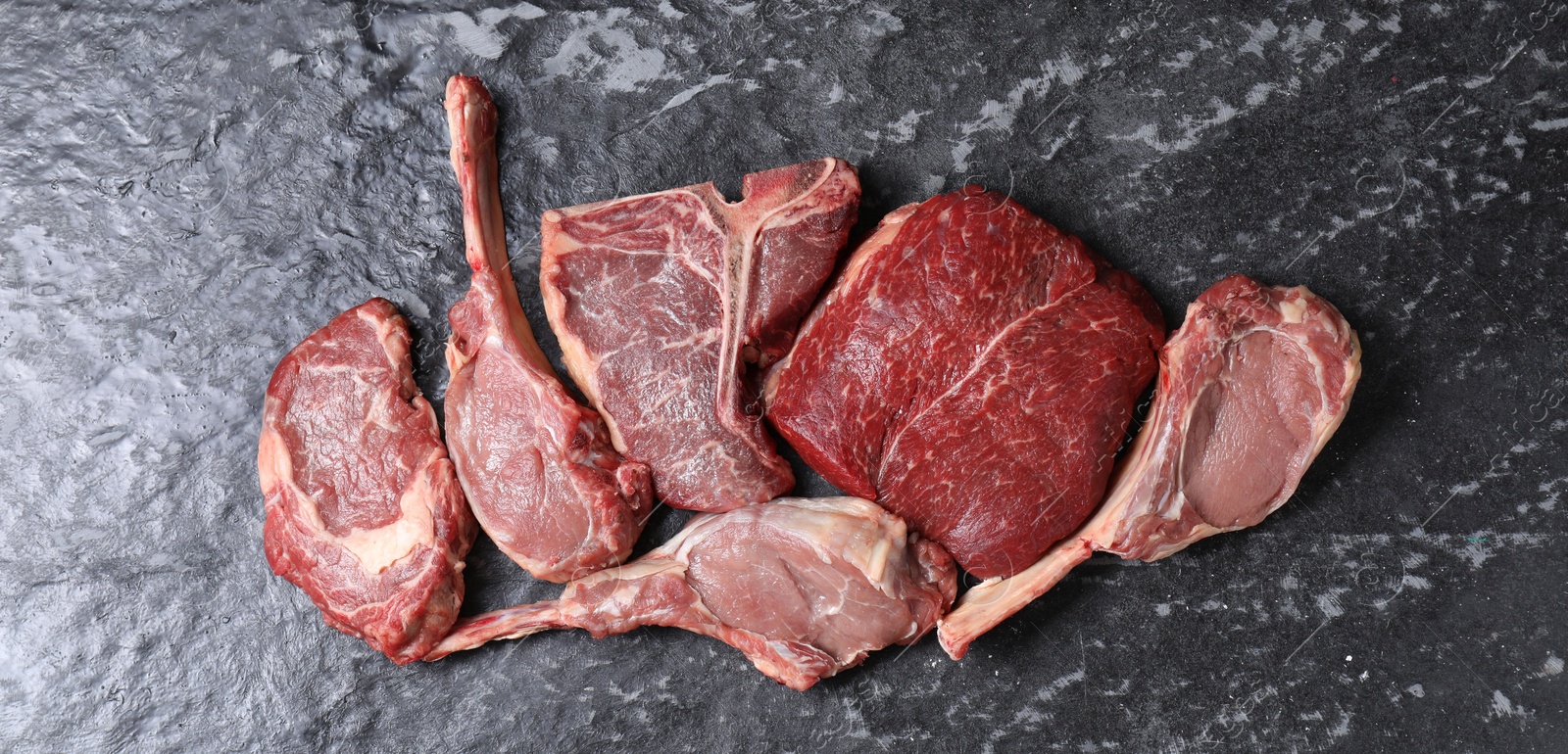 Photo of Fresh raw beef cuts on grey textured table, flat lay