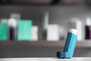 Photo of Asthma inhaler on table against blurred background. Space for text