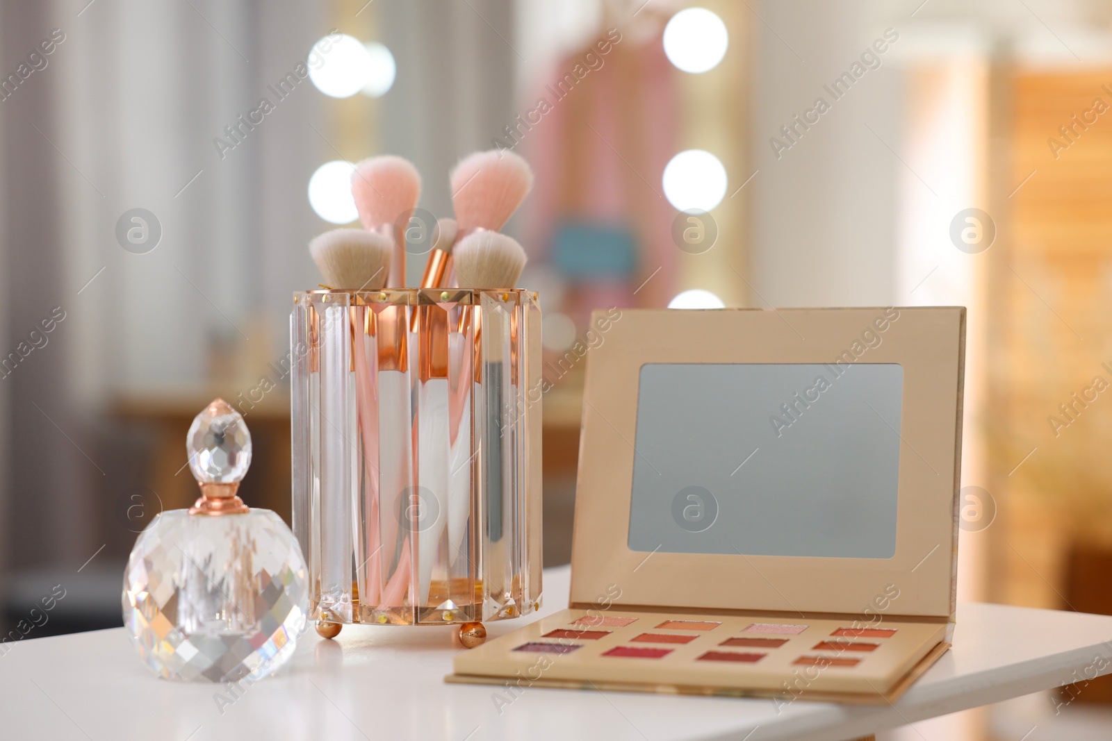 Photo of Set of brushes, eyeshadow palette and perfume on white table in makeup room
