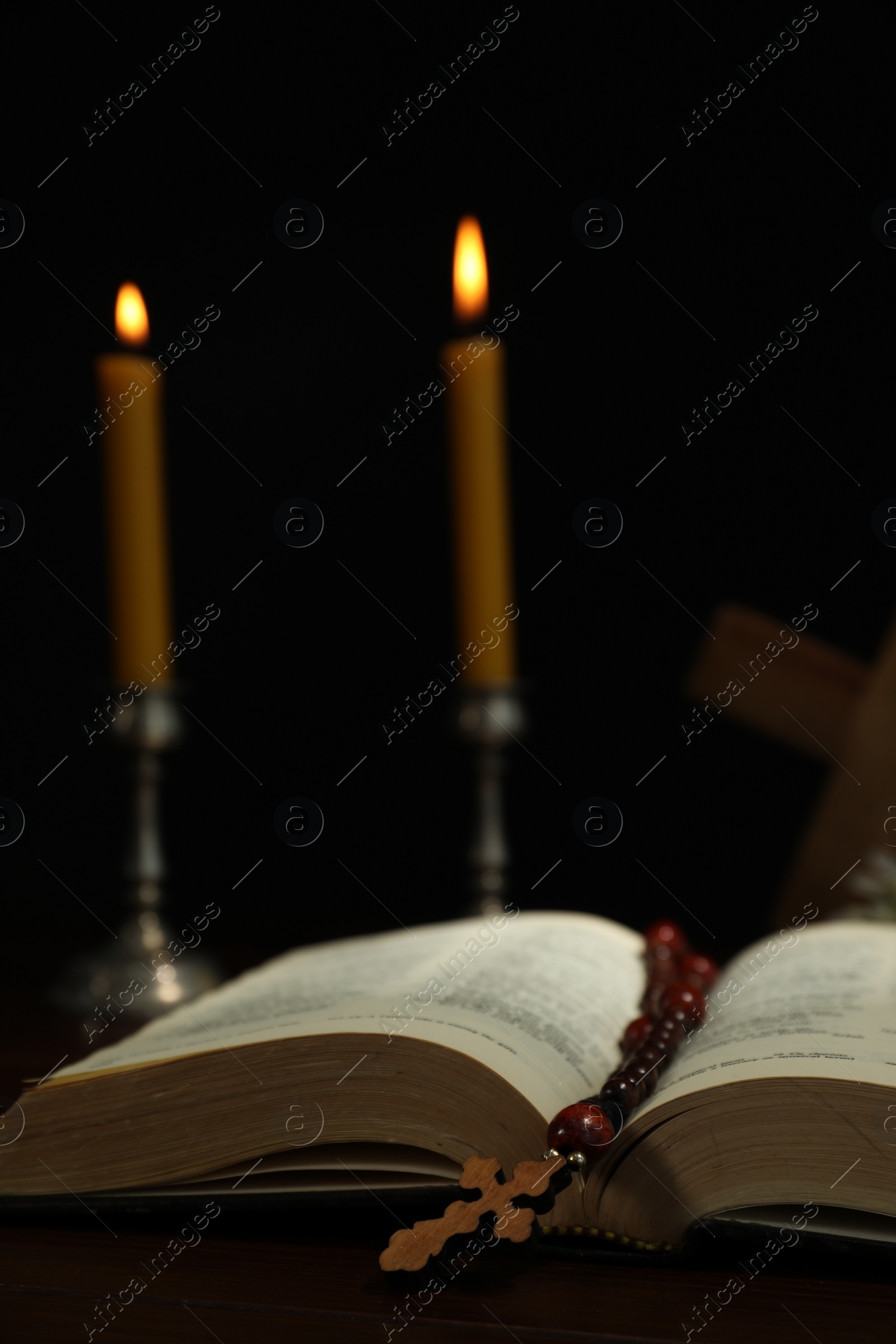 Photo of Cross, rosary beads, Bible and church candles on wooden table