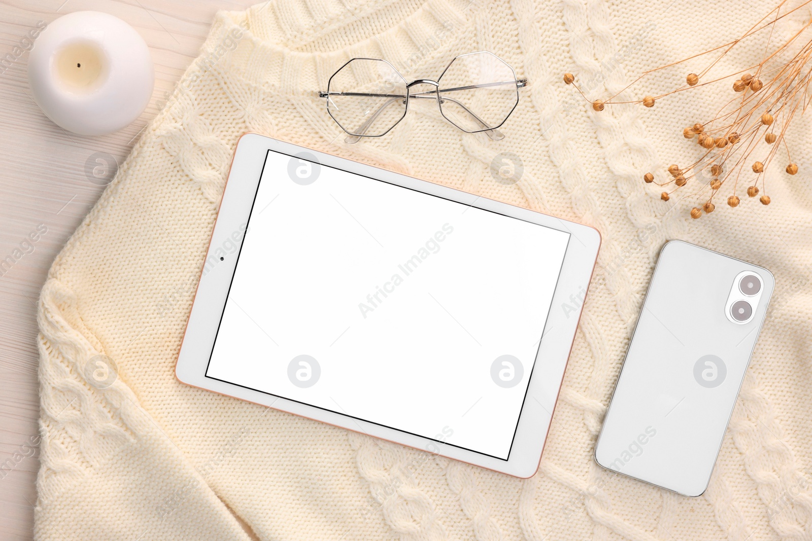 Photo of Modern tablet, glasses, smartphone, candle and sweater on white wooden table, flat lay. Space for text