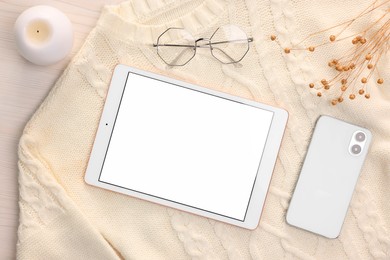 Modern tablet, glasses, smartphone, candle and sweater on white wooden table, flat lay. Space for text