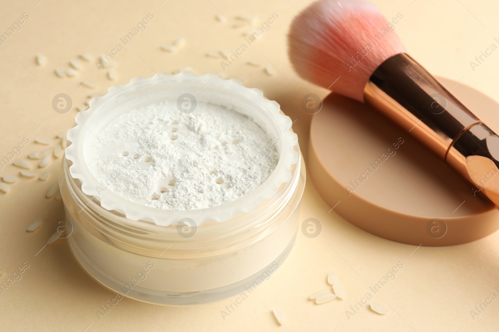Photo of Rice loose face powder and makeup brush on beige background, closeup