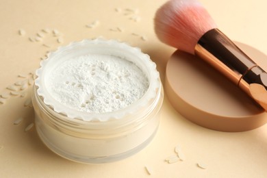 Rice loose face powder and makeup brush on beige background, closeup