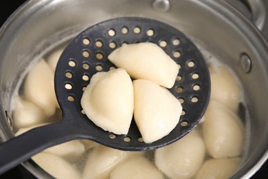 Dumplings (varenyky) with cottage cheese on skimmer over pot, closeup