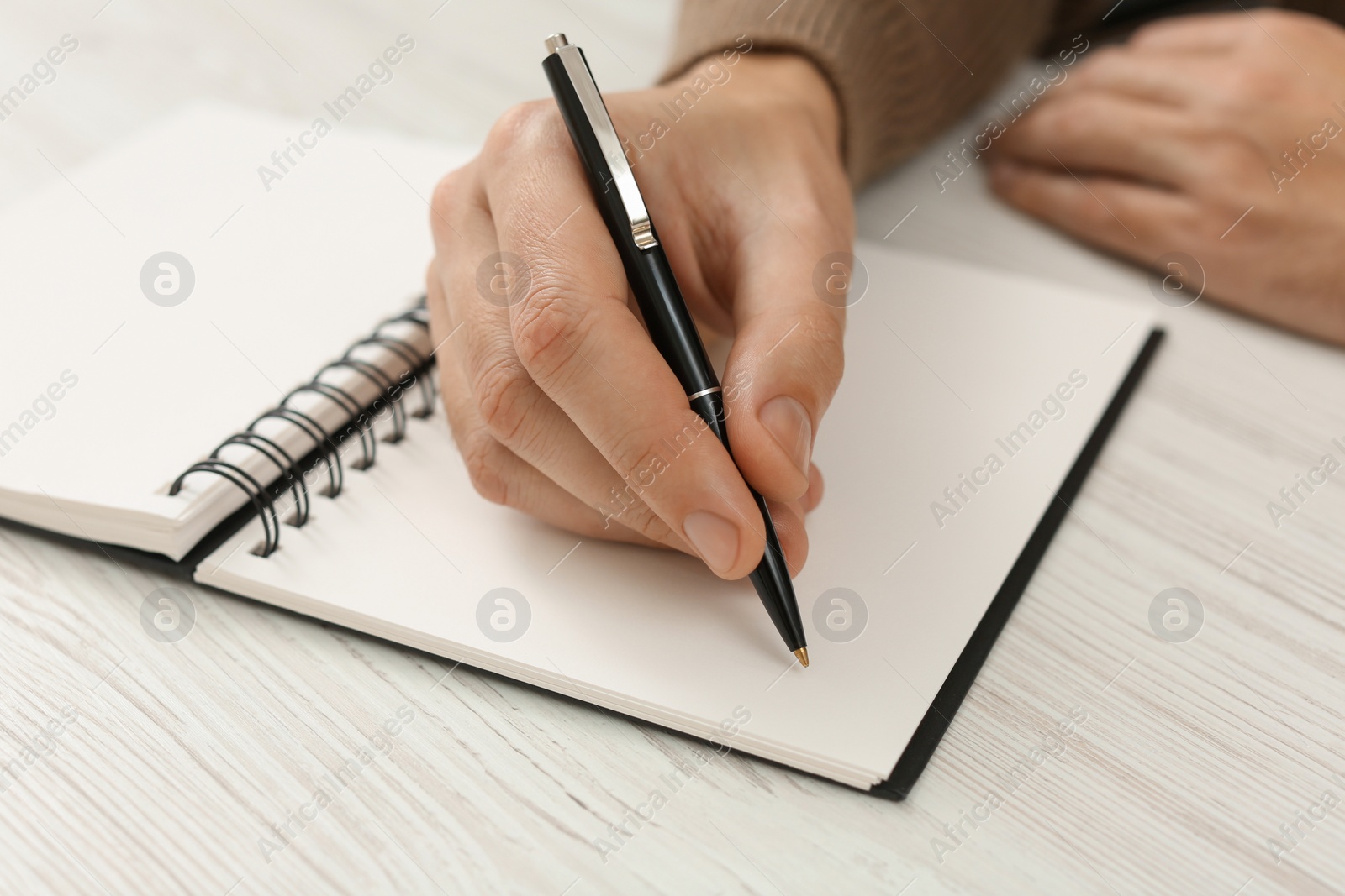 Photo of Man writing in notebook at white wooden table, closeup