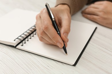 Photo of Man writing in notebook at white wooden table, closeup