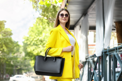 Photo of Beautiful young woman with stylish leather bag outdoors on summer day