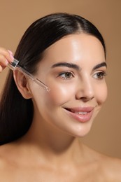 Photo of Beautiful young woman applying serum onto her face on beige background