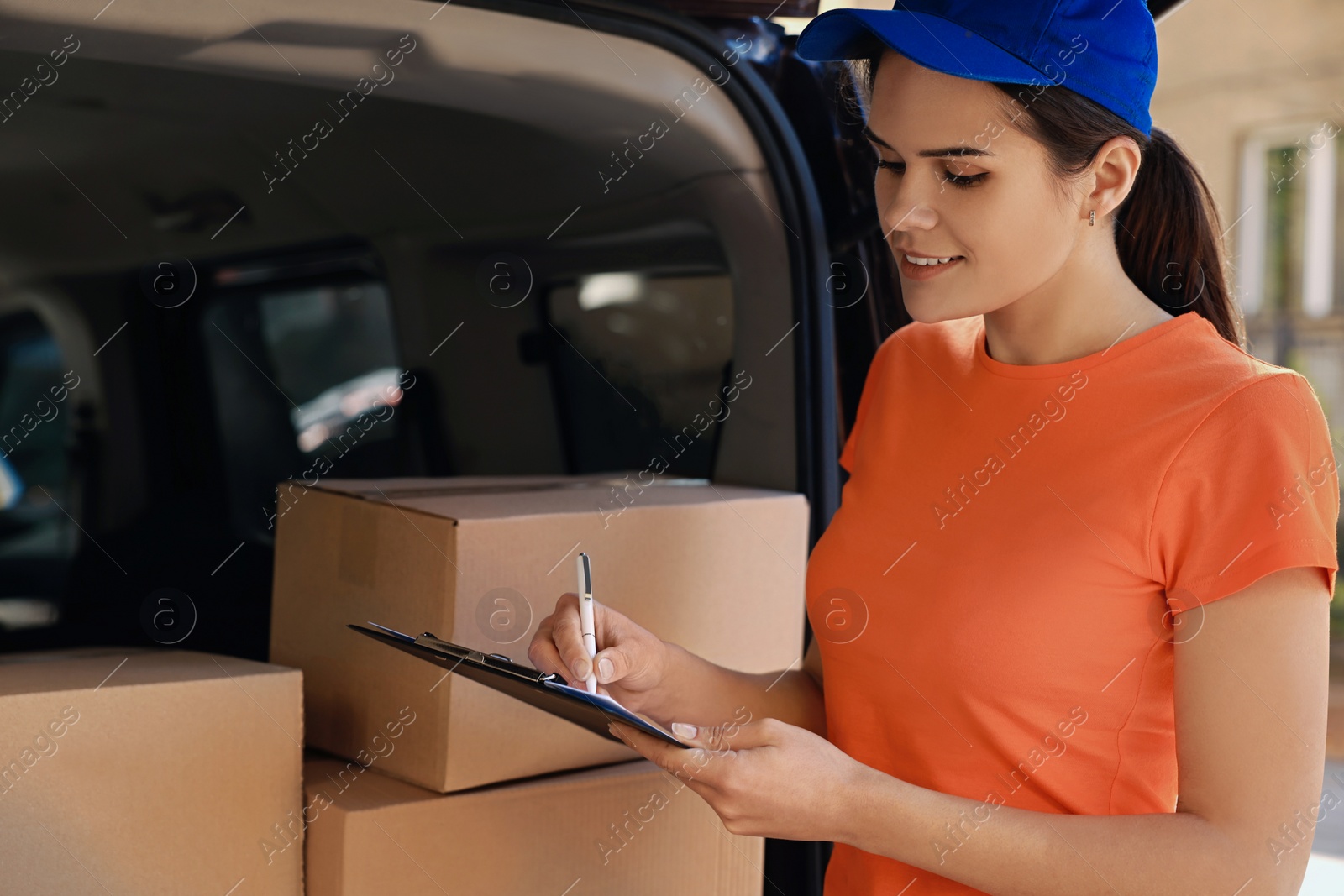 Photo of Courier writing near packages and delivery truck outdoors
