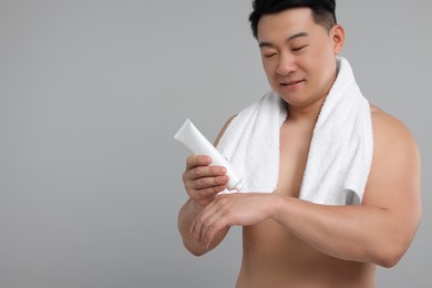 Photo of Handsome man applying body cream onto his hand against light grey background. Space for text