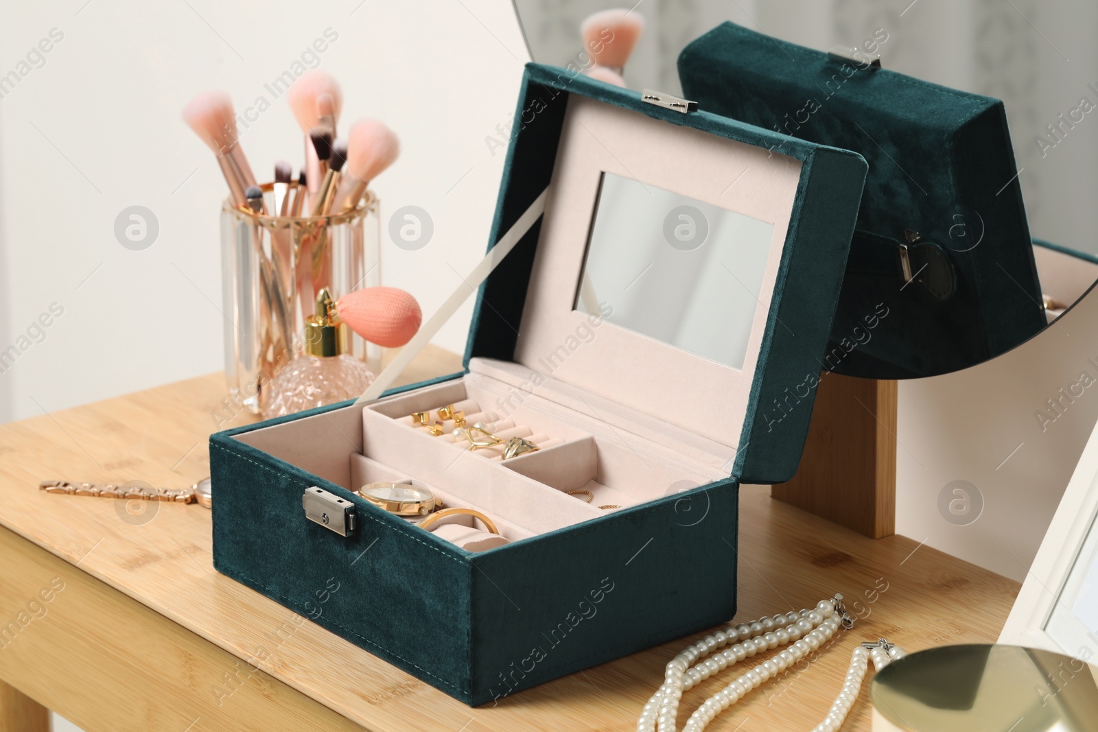 Photo of Jewelry box with many different accessories, perfume and makeup brushes on wooden table